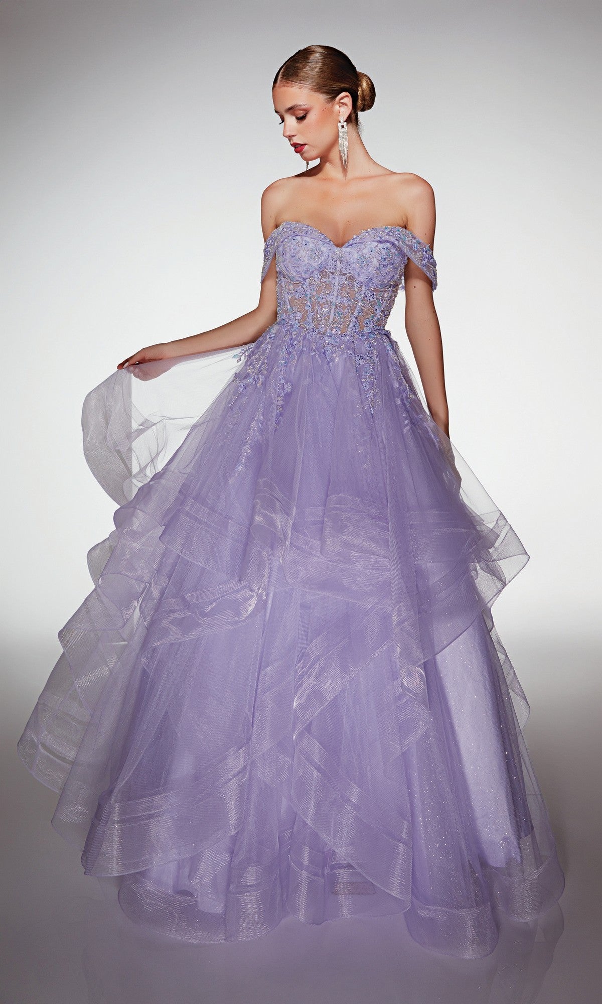 A woman in the Alyce 62207 long formal dress with a strapless, layered lavender tulle skirt and sheer floral lace bodice holds part of her prom gown and looks down.